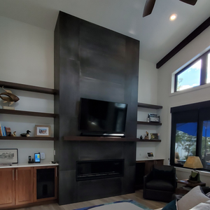 Grey and rush fireplace tile, floor to ceiling. Walnut cabinets on either side of fireplace with 3 floating shelves above. Light wall colour and light couch.