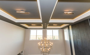 Grey coffered ceiling, white trim details, dark grey tile on right wall, and a large satin nickel chandelier.